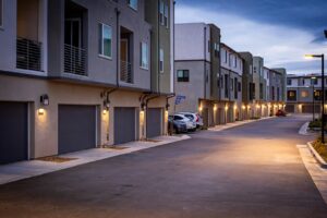 Quiet suburban street with illuminated townhouses at dusk, showcasing modern architectural style.