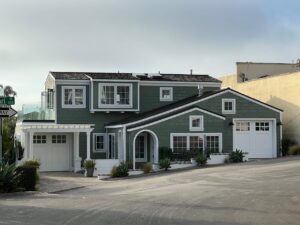 A stylish green two-story suburban house with white trim and garages on a sunny street corner.